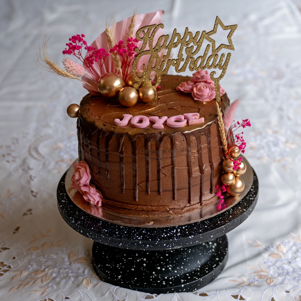 Chocolate celebration cake finished with gold spheres and fresh pink roses